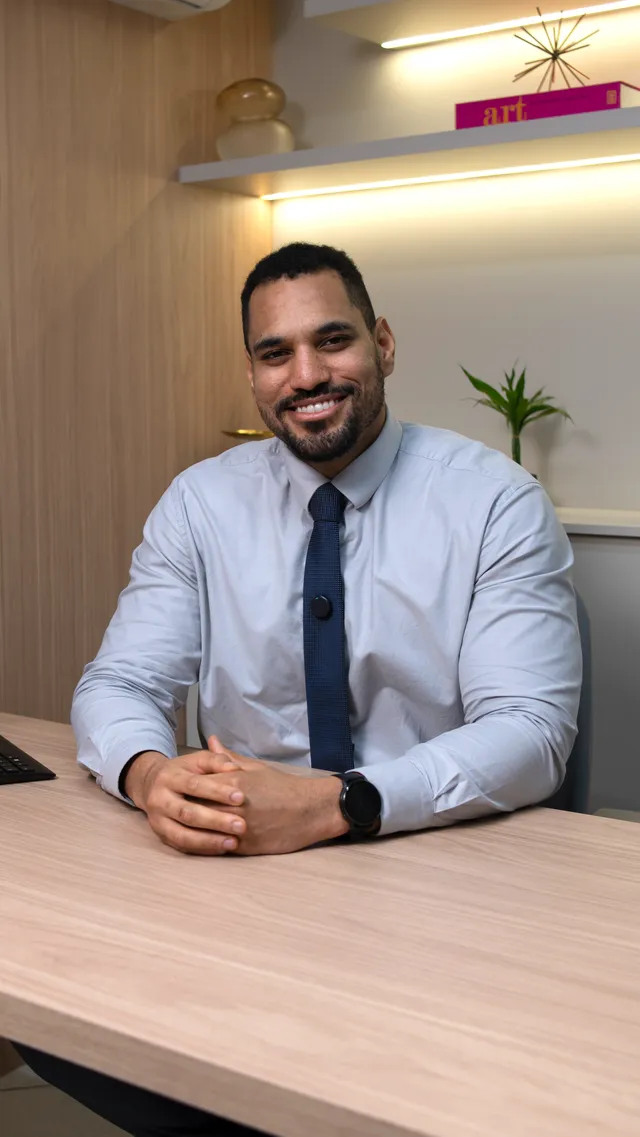 Dr. Elson Shockness, de camisa clara e gravata, sentado à mesa do consultório